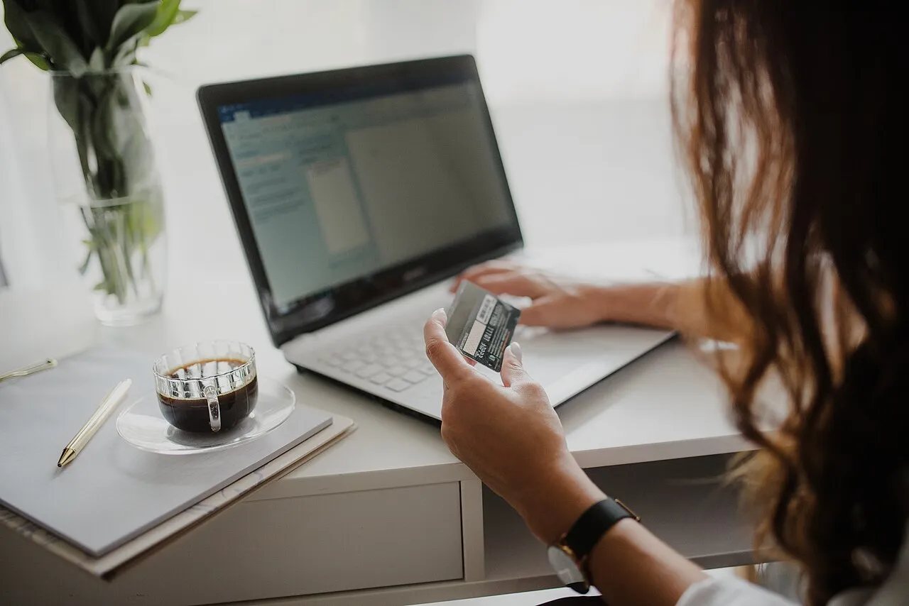 Persona revisa una tarjeta mientras usa su celular frente al computador
