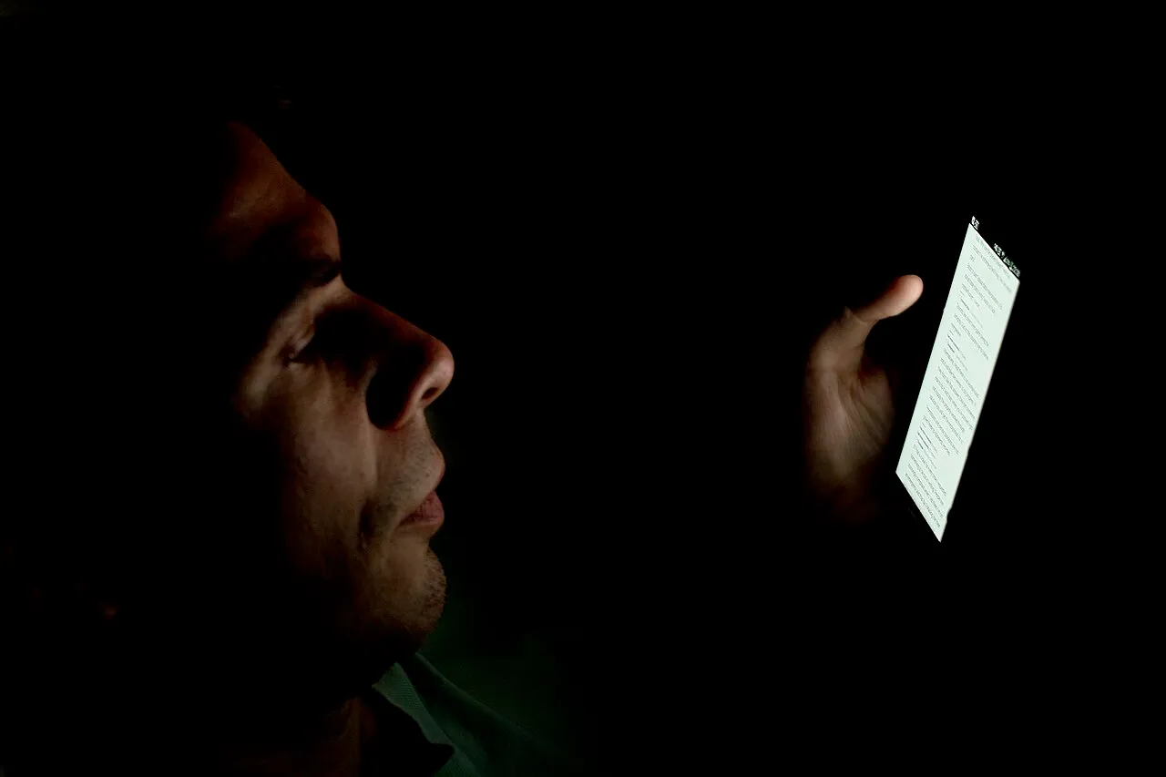 Rostro iluminado solo por la pantalla de un celular en la oscuridad