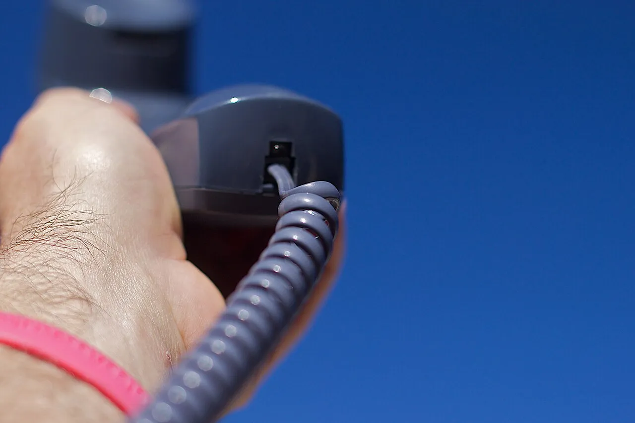 Mano sosteniendo el auricular de un teléfono fijo